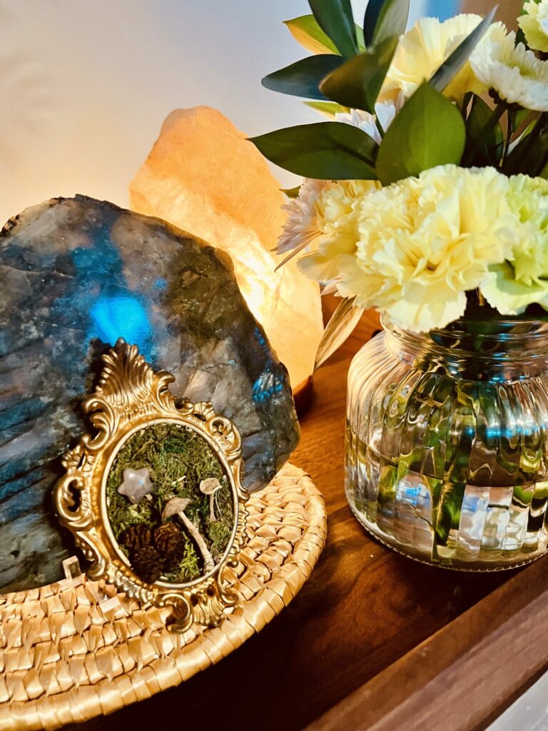 cozy home decor vignette with flowers, crystals, and warm salt lamp lighting on a wooden table