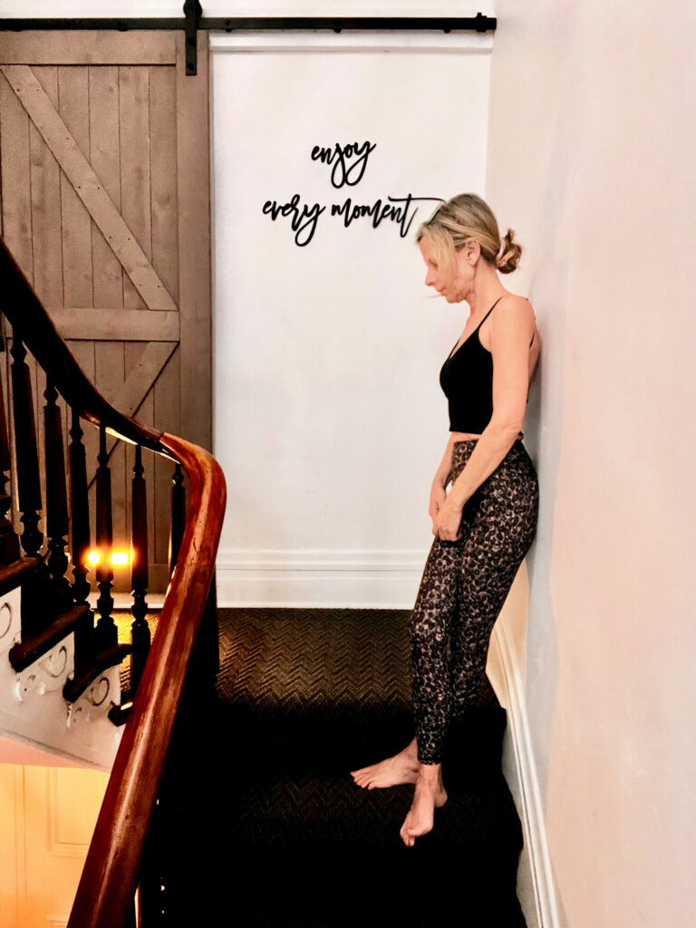 Woman standing on staircase beneath "enjoy every moment" wall sign in cozy home interior