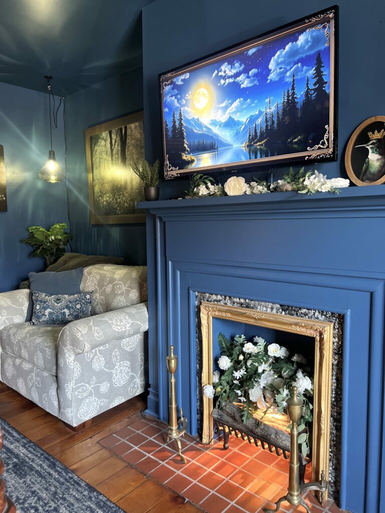 blue painted fireplace with brass surround, floral arrangement and cozy seating in a color drenched moody bedroom
