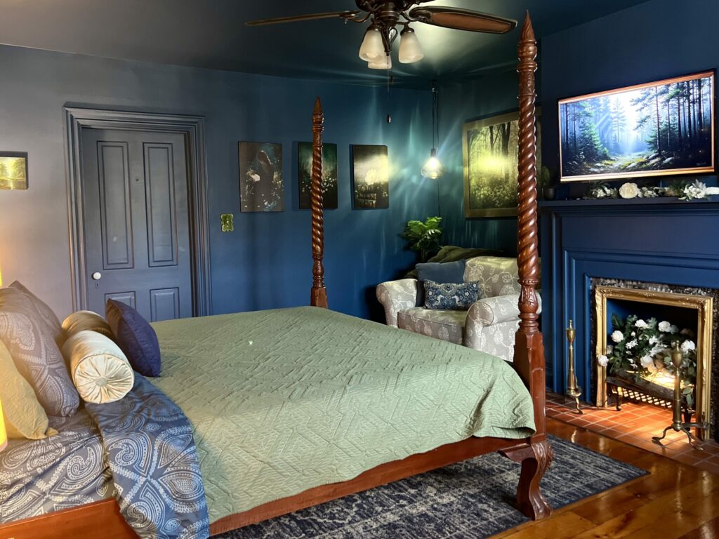 color drenched blue bedroom with four poster bed, cozy fireplace and layered blue and green bedding